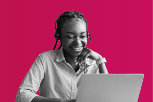 A lady with a headset on, smiling at a laptop.